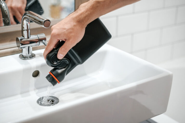 Hand pouring bottle of liquid chemical drain cleaner down bathroom sink drain